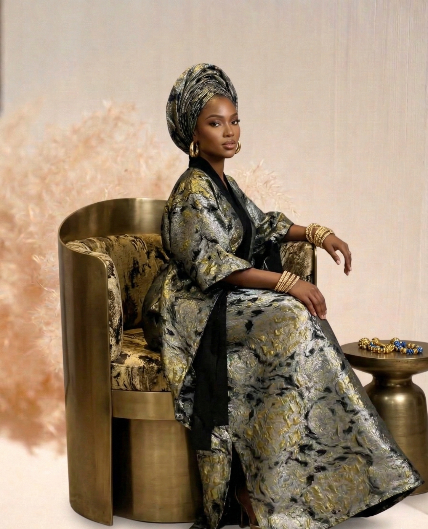Woman in a patterned outfit sitting on a gold chair with a soft, neutral background
