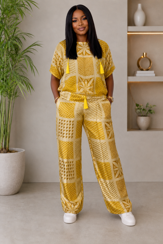 A woman modeling a matching yellow and beige patterned lounge set consisting of a short-sleeve top and wide-leg pants, styled with white sneakers in a modern indoor setting.