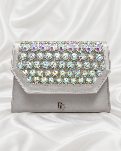 A silver clutch bag embellished with rows of iridescent round rhinestones across the front flap,