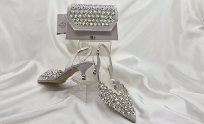 A silver bridal shoe set with matching accessories, including pointed-toe slingback heels and a matching clutch bag, both heavily embellished with iridescent rhinestones.